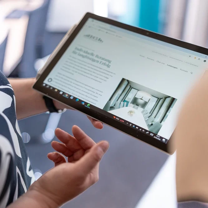 Eine Hand hält ein Tablet, auf dessen Bildschirm eine Website mit Bildern und Text zu sehen ist.